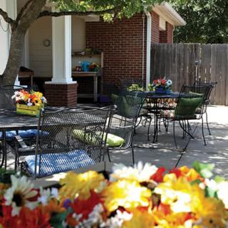 A cozy outdoor patio with tables and chairs surrounded by colorful flowers.