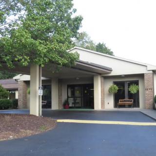 A building entrance with a covered walkway, surrounded by trees and landscaping.