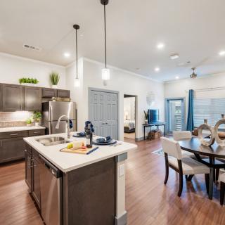 A modern open-concept kitchen and dining area featuring pendant lighting and wood flooring.