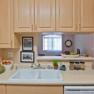 A modern kitchen with light wood cabinets, a double sink, and various items on the countertop.