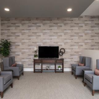 A modern living room with stylish seating and a TV against a brick accent wall.