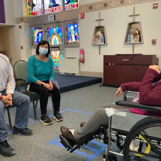 A group of individuals engaged in a conversation in a community space, with one person seated in a wheelchair.