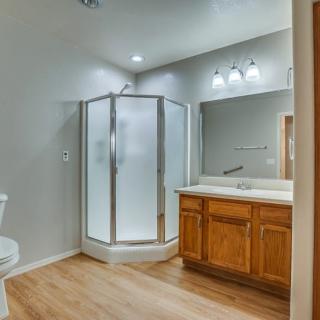 A modern bathroom with a glass shower enclosure, wooden cabinets, and a large mirror.