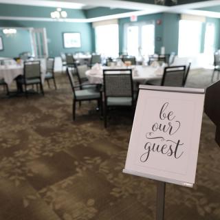 A dining area with neatly arranged tables and a welcoming sign that reads 'be our guest'.