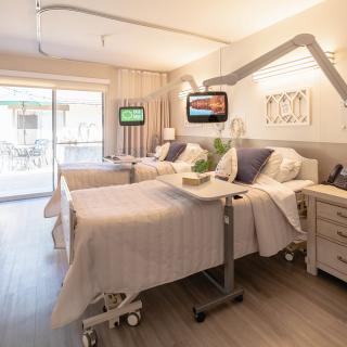 A modern hospital room with two beds, equipped with televisions and medical equipment, designed for patient comfort.