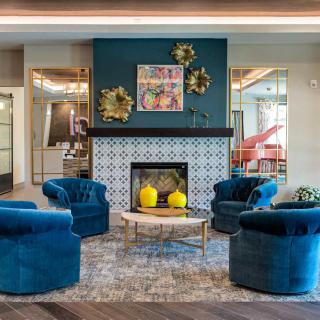 A modern living room featuring a central fireplace surrounded by blue armchairs and decorative elements.