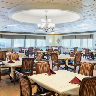 A spacious dining room with elegantly set tables and a central chandelier.
