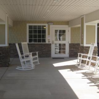 A covered porch with white rocking chairs and a glass door.