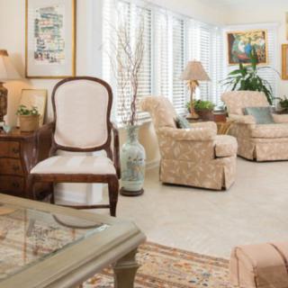 A cozy living room with traditional decor, featuring armchairs, lamps, and natural light streaming through the windows.