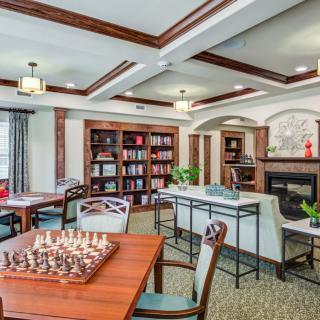 A cozy library room featuring a chess set, bookshelves, and comfortable seating by the fireplace.