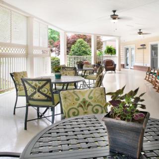 A spacious patio with tables, chairs, and ceiling fans surrounded by greenery.