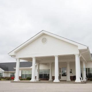 A white building with columns and a covered entrance under a cloudy sky.