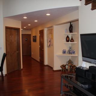 A cozy living area with wooden floors, recessed lighting, decorative shelves, and a television.