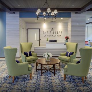 A modern lobby with green chairs, a central table, and a reception desk at The Pillars.