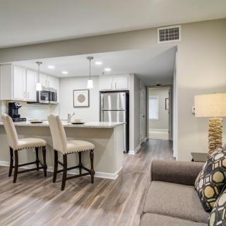 A modern open floor plan living area with a view into the kitchen, featuring bar stools, neutral tones, and recessed lighting.