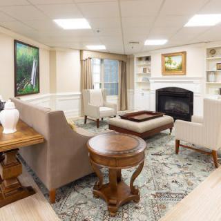 A cozy living room with elegant furniture and a fireplace, featuring artwork and decorative elements.