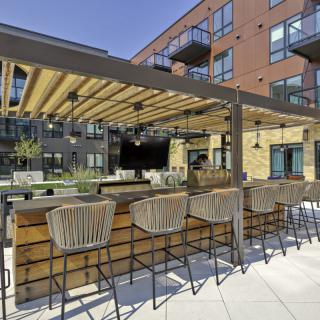 An outdoor bar with modern seating and a pergola, located in an apartment complex courtyard.