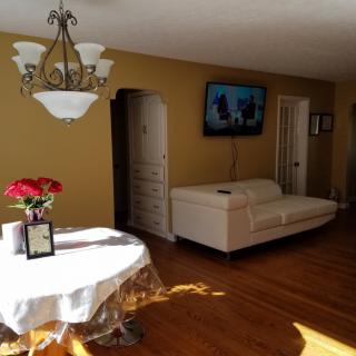 A cozy living room with a white sofa, wall-mounted TV, and a table with red flowers.