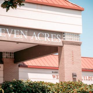 A sunny day view of a building with a red roof and signage reading 'SEVEN ACRES'.
