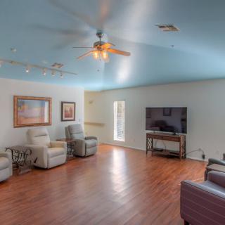 Spacious living room with wood flooring and comfortable seating, featuring a large TV and ceiling fan.