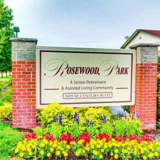 Entrance sign for Rosewood Park Senior Retirement & Assisted Living Community surrounded by colorful flowers.