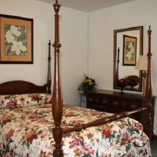A cozy bedroom featuring a four-poster bed with floral bedding, a dresser with a mirror, and framed artwork on the wall.