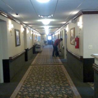A hallway with carpeted floor and overhead lighting, featuring a person in the distance.