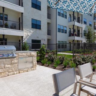 A modern apartment complex with an outdoor patio featuring a grill and seating area under an umbrella.
