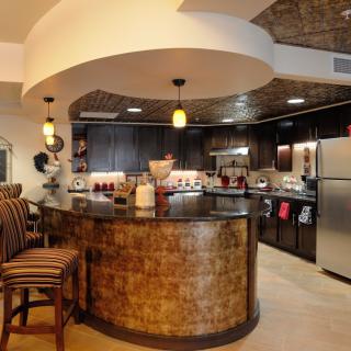 A modern kitchen featuring a stylish bar counter with pendant lighting, stainless steel appliances, and a cozy seating area.
