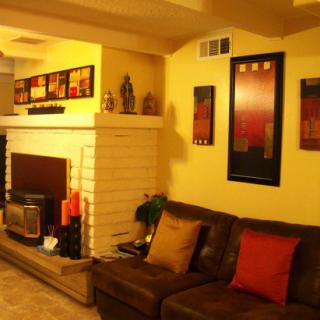 A cozy living room with a sofa, artwork on the walls, and a fireplace under warm lighting.