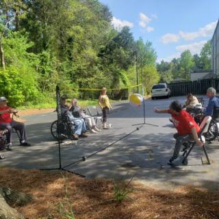 People enjoying a sunny day playing badminton outdoors, including participants in wheelchairs.