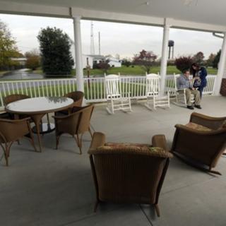 A cozy outdoor porch with multiple seating options, including wicker chairs and rocking chairs, provides a relaxing environment for people to enjoy the view.