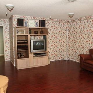 A vintage-style living room featuring a television and bookshelf, adorned with floral wallpaper and wooden flooring.