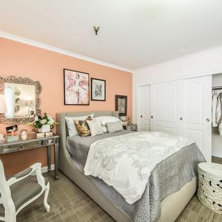 A cozy bedroom with a soft color palette featuring a bed, vanity, and closet space.