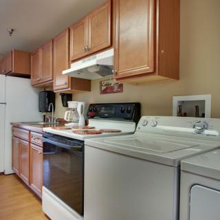 A kitchen with wooden cabinets, featuring appliances like a washer, dryer, and oven.