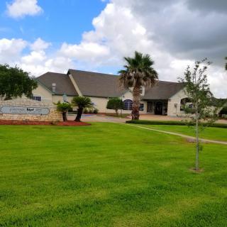 A scenic view of a building surrounded by a well-maintained lawn and palm trees under a cloudy sky.