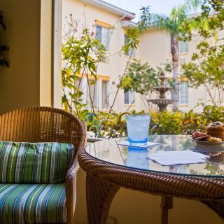 A cozy patio setting with a wicker chair and table overlooking a sunny courtyard.