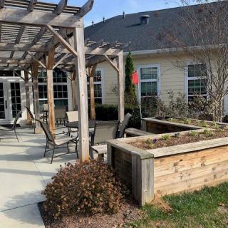 A patio area with a pergola, outdoor seating, and raised garden beds next to a building.