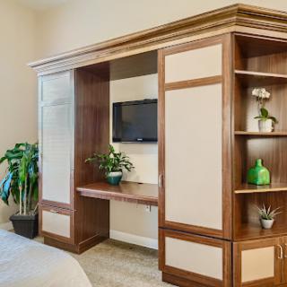 A cozy living space featuring modern wooden furniture with a mounted TV and decorative plants.
