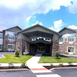 A modern building with a prominent entrance and landscaped surroundings under a partly cloudy sky.