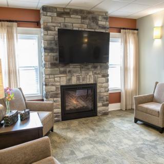 A cozy living room featuring a stone fireplace with a television mounted above, surrounded by comfortable armchairs and large windows.
