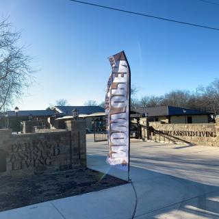 A feather flag sign reading 'NOW OPEN' at the entrance of a property.
