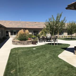 A serene outdoor space featuring a well-maintained lawn, seating area, and clear blue skies.