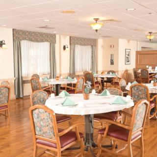 A well-arranged dining room with tables and chairs set up for guests, featuring decorative napkins and a cozy atmosphere.