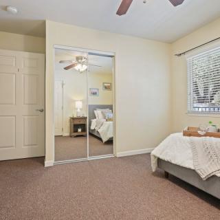 A cozy bedroom with a ceiling fan, mirror closet, and natural light.