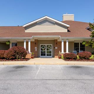 An exterior view of a brick building with a gabled roof and pillars at the entrance.