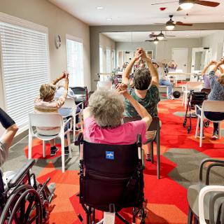 A group of elderly individuals participating in a seated exercise session at a community center.