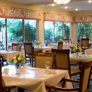 A cozy restaurant dining room with elegantly set tables and large windows offering a garden view.