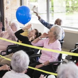 A group of seniors engaging in a fun indoor activity with a blue balloon.