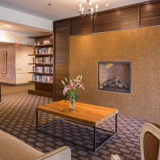 A cozy lounge area with a fireplace and a bookshelf, featuring a wooden table with a floral arrangement.